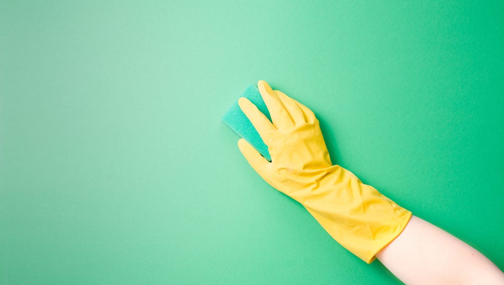 a female hand in a yellow rubber glove washes a plain surface with a green paralon sponge