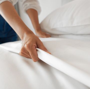 female hand set up white bed sheet in bedroom
