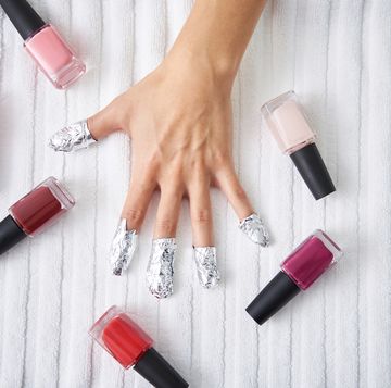 female hand with strips of foil on fingers and nail polishes on towel