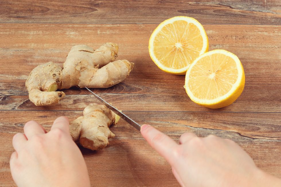 female hands cut into pieces ginger root for a drink made from fresh lemon and ginger on brown wooden background handmade drink