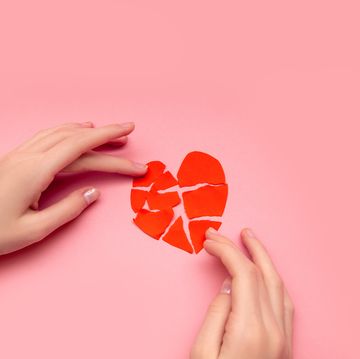 female hands gluing together broken heart, pieces of torn red valentine on pink background the concept of disappointment in love, salvation of relationships close up photo