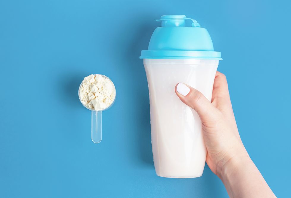 female hands hold bottle of protein shake and a measuring spoon with protein powder, top view