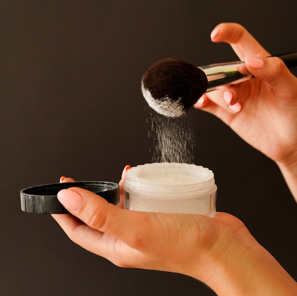 female hands holding jar of powder and cosmetic brush on black background