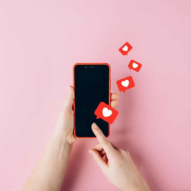 female hands holding red mobile phone with many social media likes on pink background
