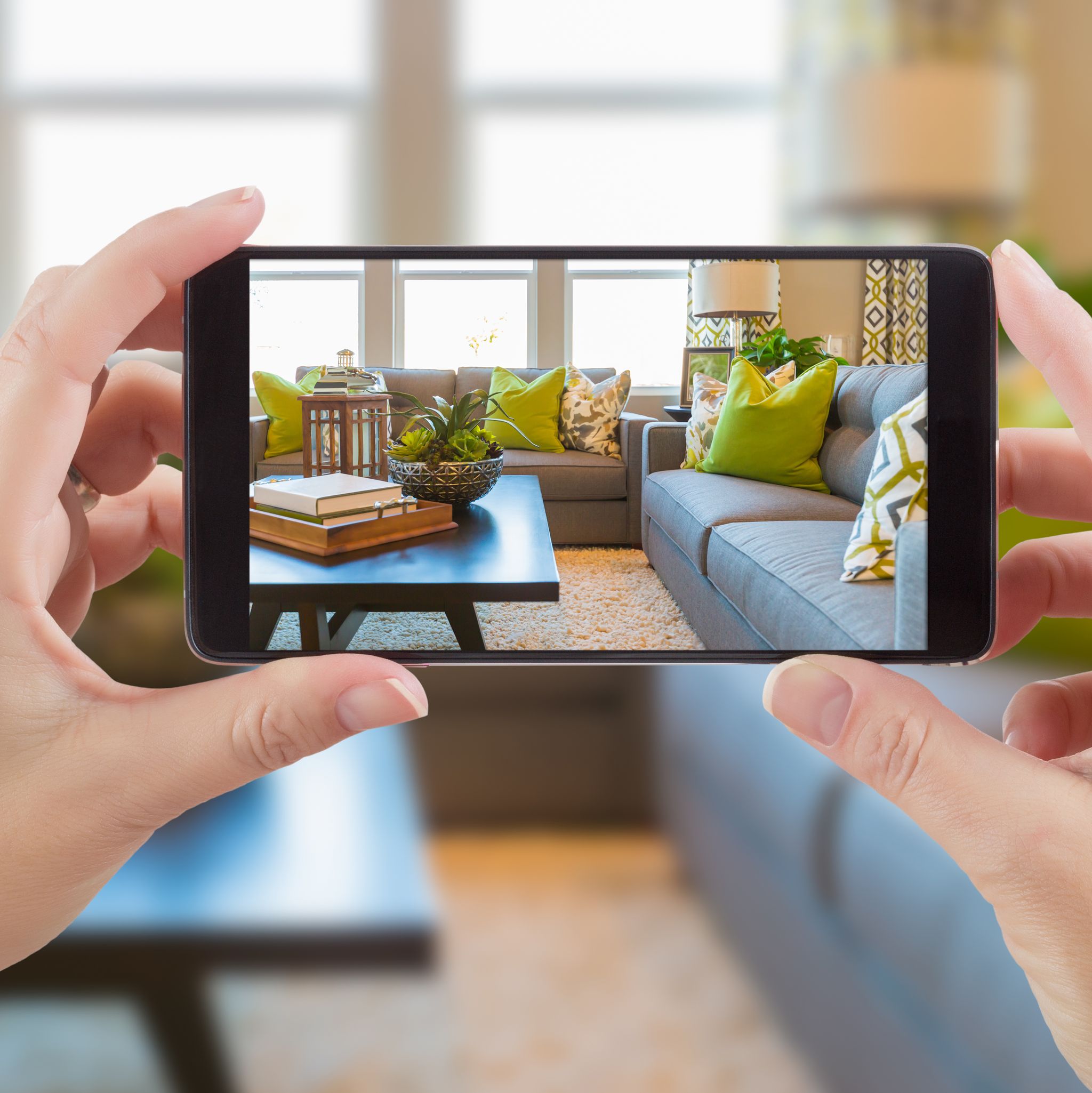 female hands holding smart phone displaying photo of house interior living room behind