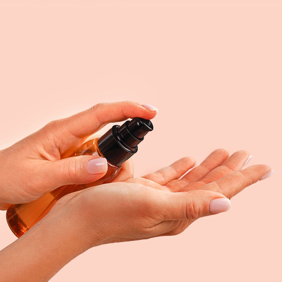 female hands holds  bottle with natural organic face serum or essential organic oil on trendy peach pink color background