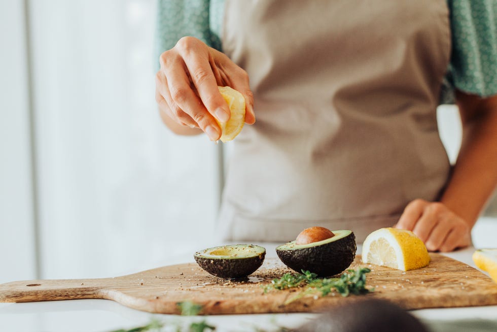 female hands squeezing lemon on avocado while preparing healthy meal