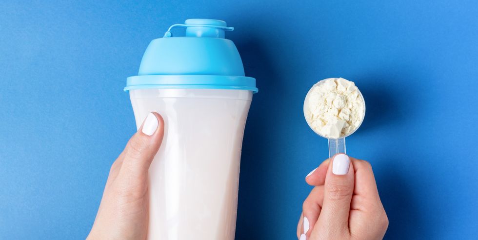 female hands with white manicure hold bottle of protein shake and a measuring spoon with protein powder, top view