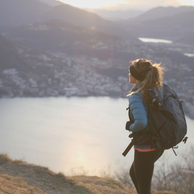 female hiker walks above lake and european alps