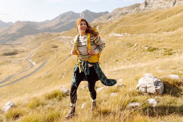 female hiker with colorful backpack feeling freedom among majestic mountains.