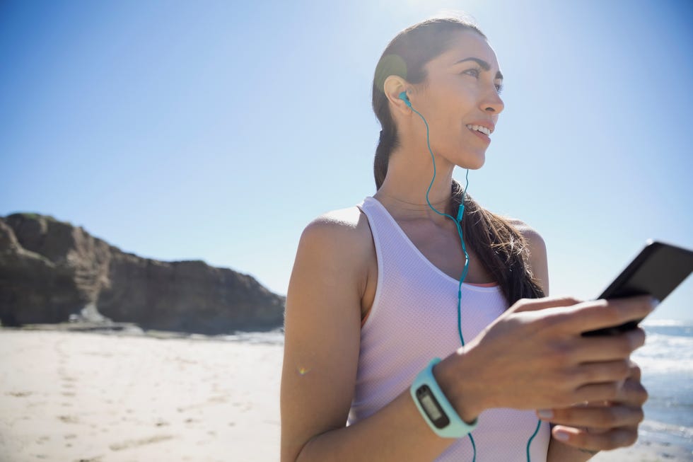 Female Latina runner listening to music with mp3 player and headphones on sunny beach