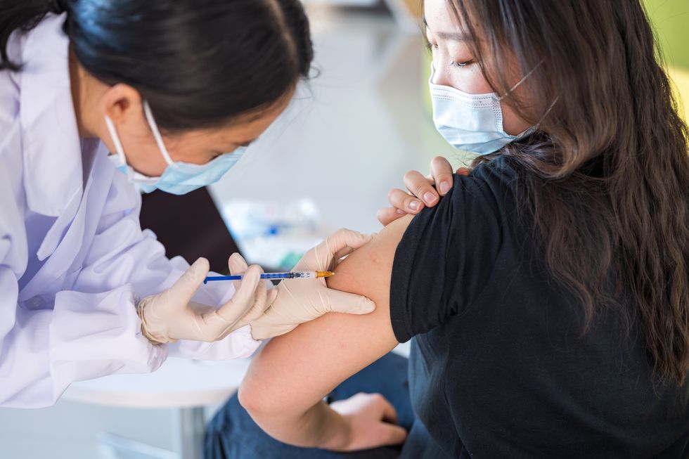 a female nurse is vaccinating a young asian woman