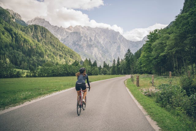 female road biker rides along sunny country road