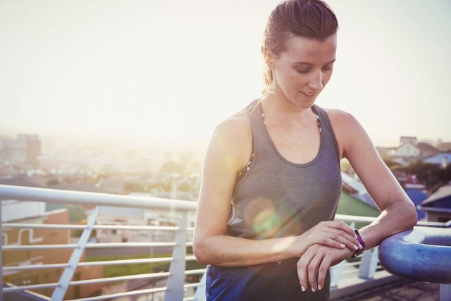 Female runner resting checking smart watch fitness tracker on sunny urban footbridge