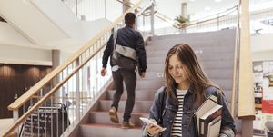 Female student using mobile phone while man walking up on steps in university