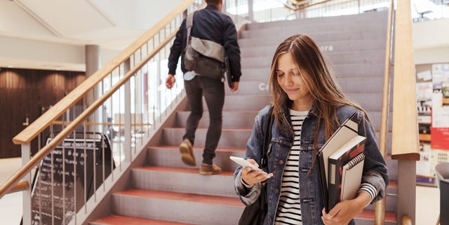 Female student using mobile phone while man walking up on steps in university