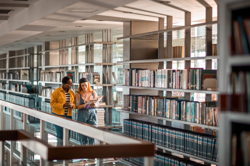 female students talking about a book in a library