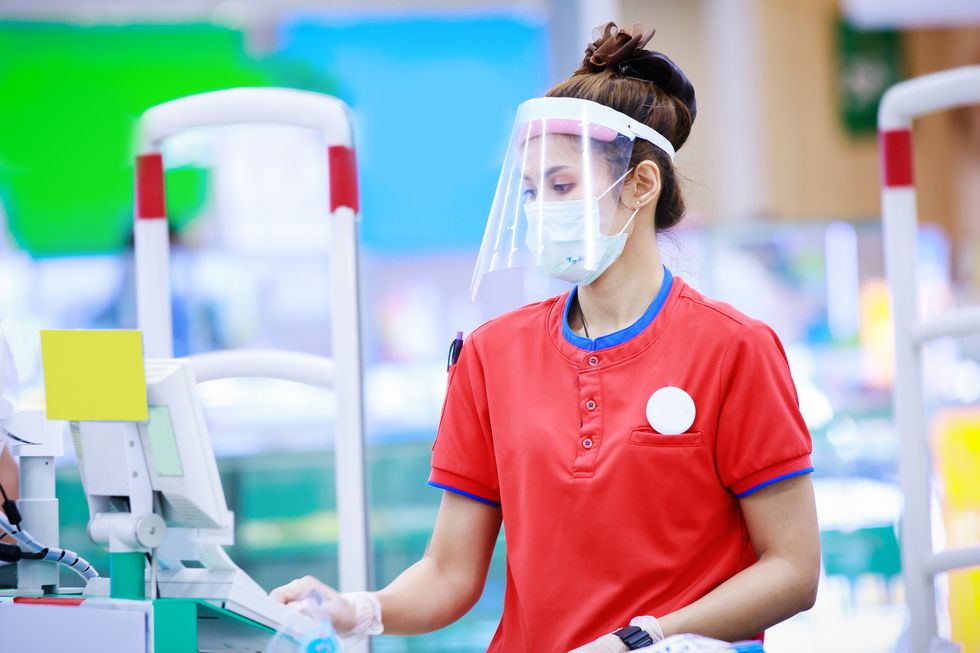 female supermarket cashier in medical protective mask and face shield working at supermarket