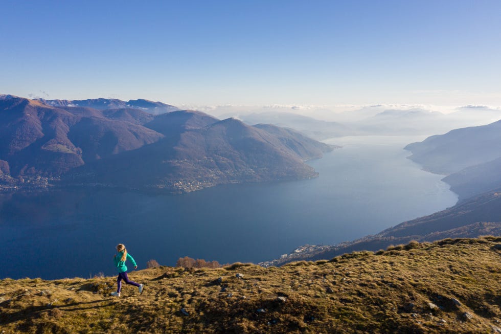 female trail runner runs along grassy mountain ridge above lake