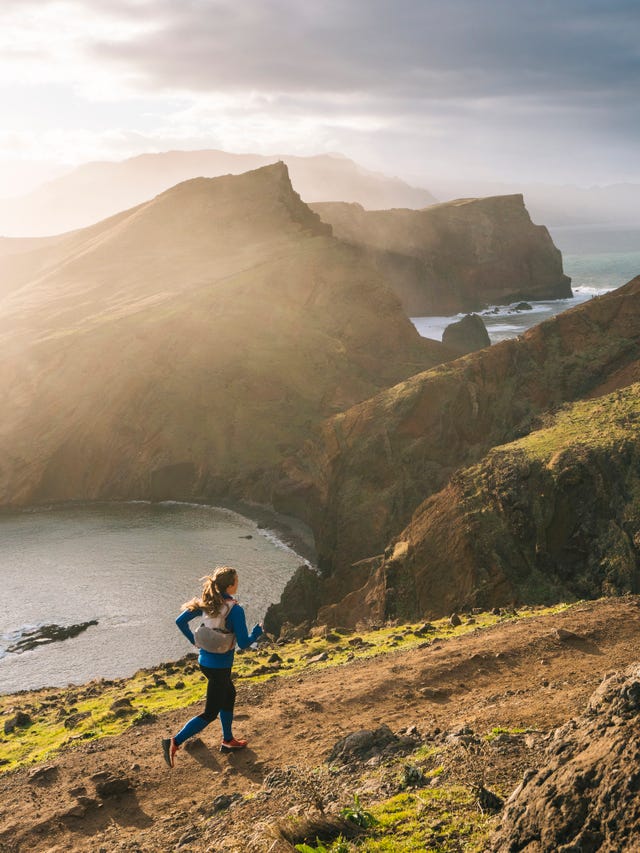 female trail runner traverses trail above coastline, cliffs