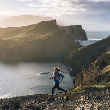female trail runner traverses trail above coastline, cliffs