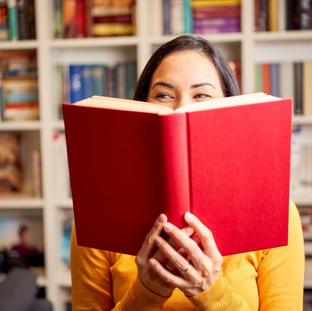 female young behind book with face covered for a red book while smiling