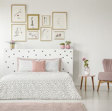 feminine bedroom interior with white walls, polka dot bedding, pink elements and fashion drawings gallery in golden frames