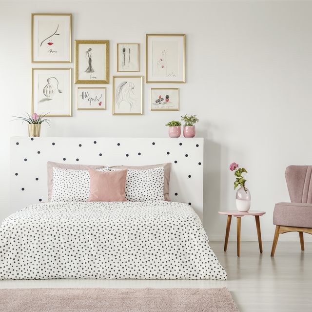 feminine bedroom interior with white walls, polka dot bedding, pink elements and fashion drawings gallery in golden frames