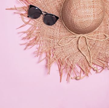 feminine staraw hat with wide fields and sunglasses on the pink background