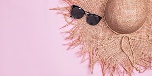 feminine staraw hat with wide fields and sunglasses on the pink background
