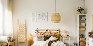 lamp above bed with beige bedsheets in warm bedroom interior with ladder, posters and wood