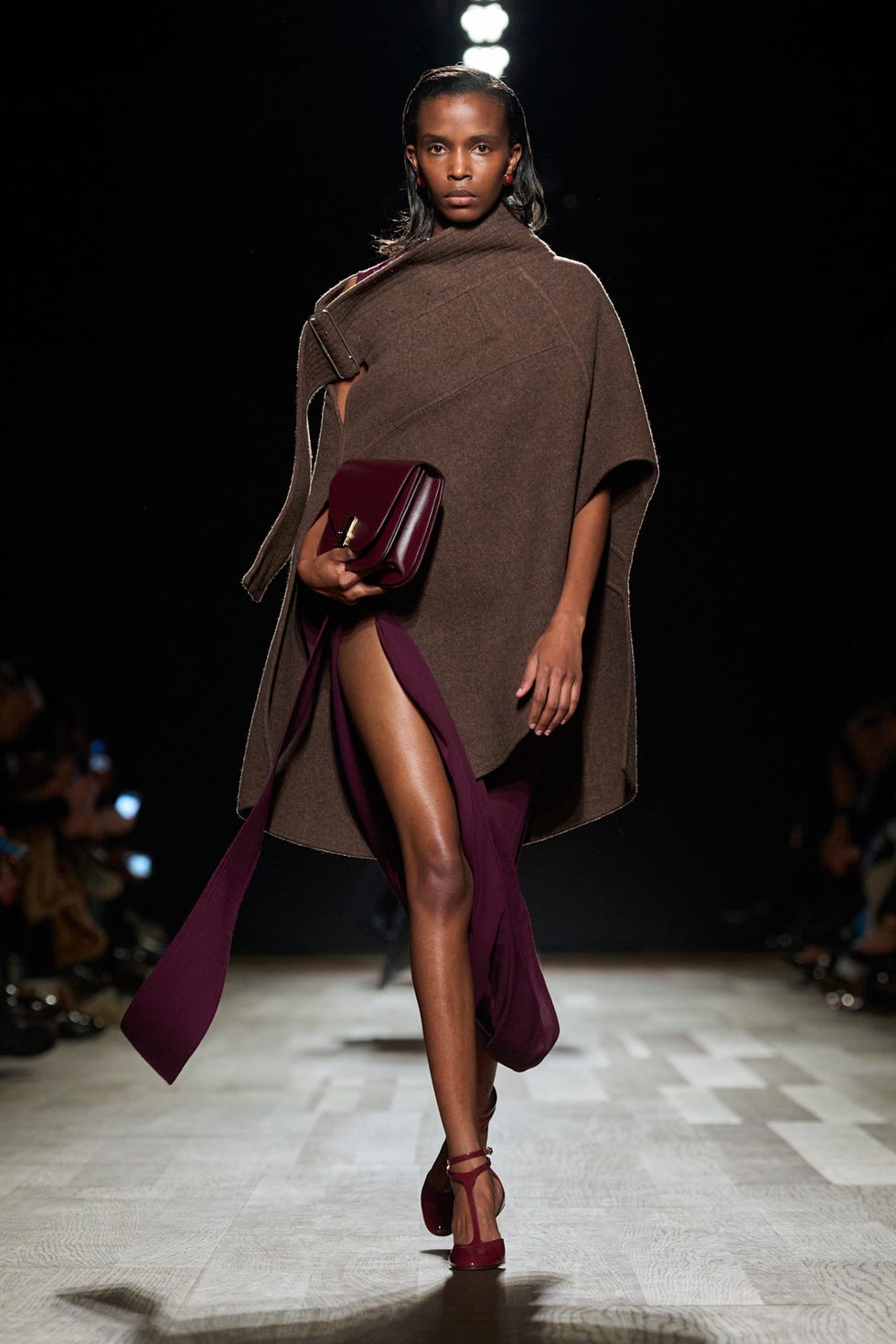 Fashion model walks the runway in a brown cape and burgundy gown with matching accessories