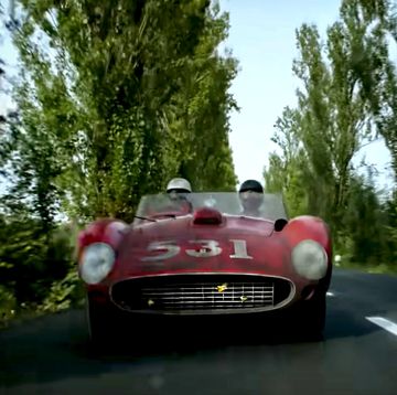 a vintage ferrari approaches the camera along a narrow tree lined road in a still from michael mann's upcoming film