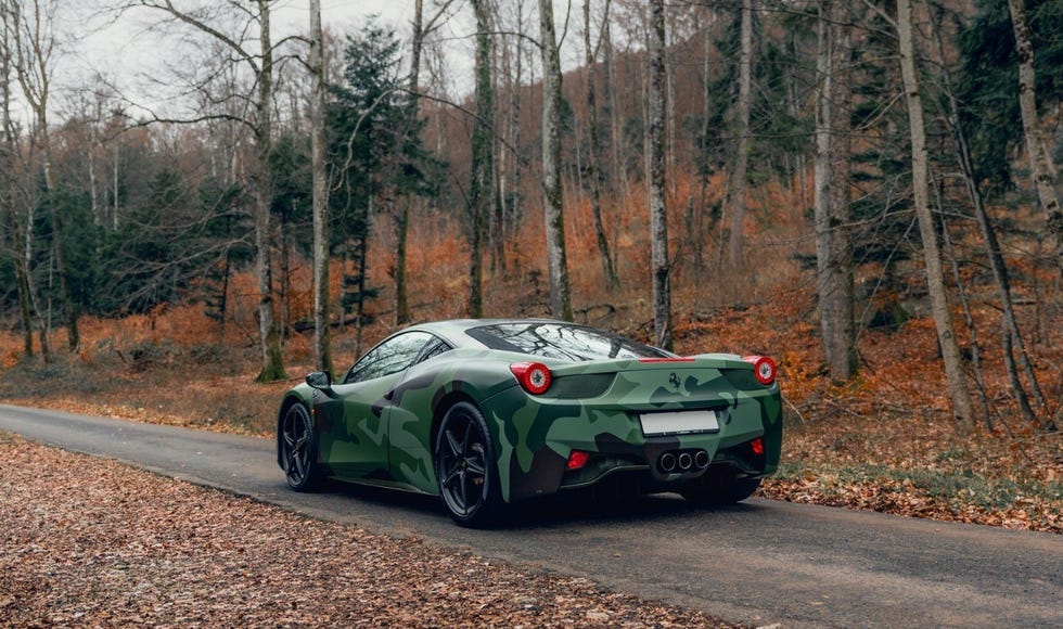 a green sports car on a road with trees on either side