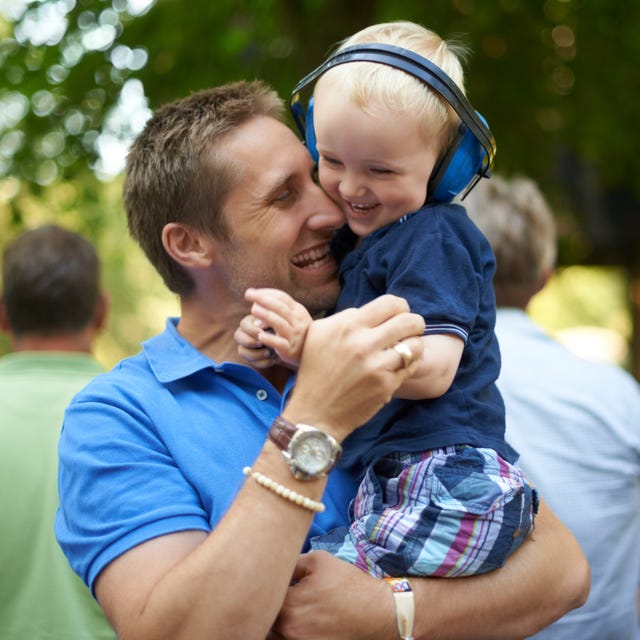 Father and son at a festival, son wearing noise cancelling headphones festival fun with father and son each in a blue shirt, baby wearing blue noise cancelling headphones