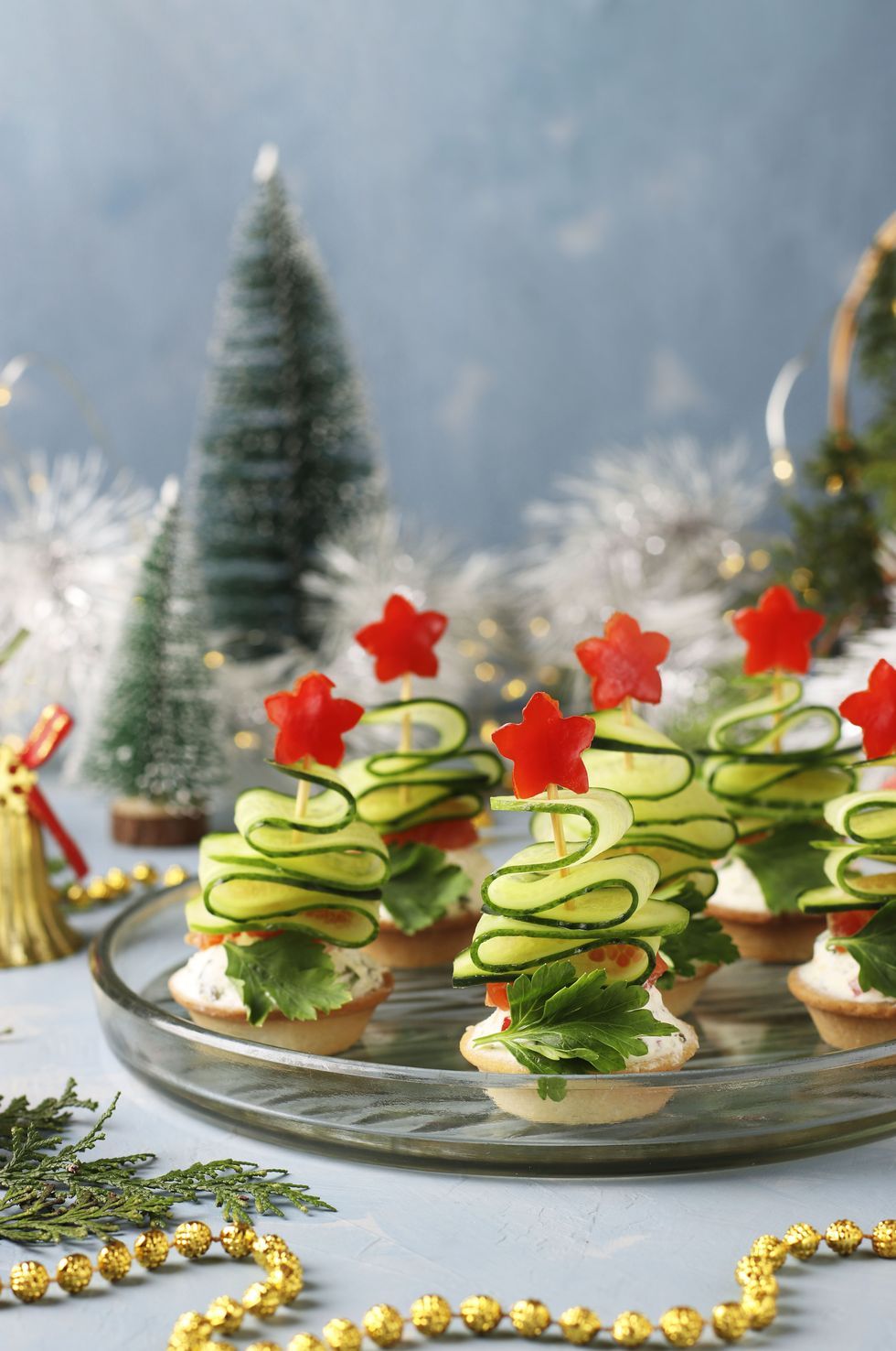 festive canapes in the shape of christmas trees made of cucumbers and stars of bell pepper on a light blue background with two glasses of wine, closeup