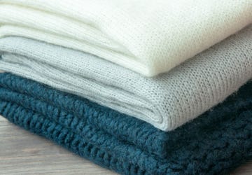 A few stacked warm knitted sweaters, lying on a wooden background. The concept of  warm.