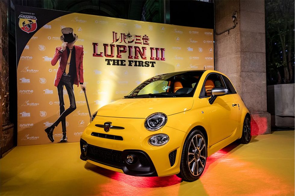 yellow fiat parked in front of lupin poster
