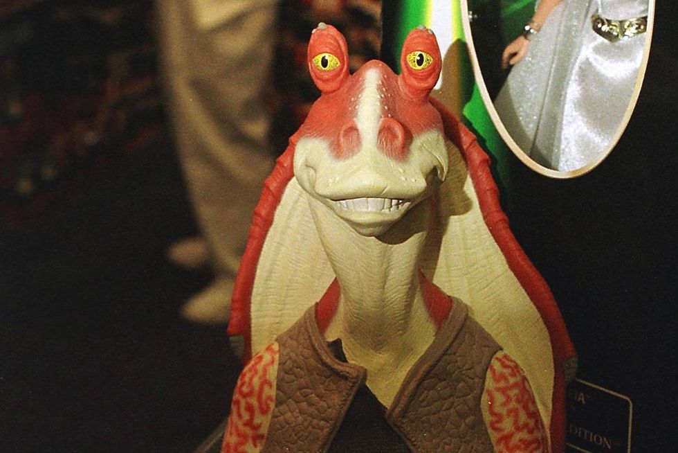 a toy of the jar jar binks star wars character on a shelf, in front of a boxed princess leia doll