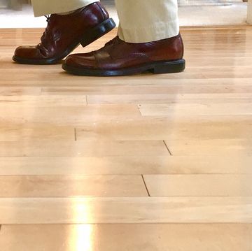 a person's feet in black shoes on a wooden floor
