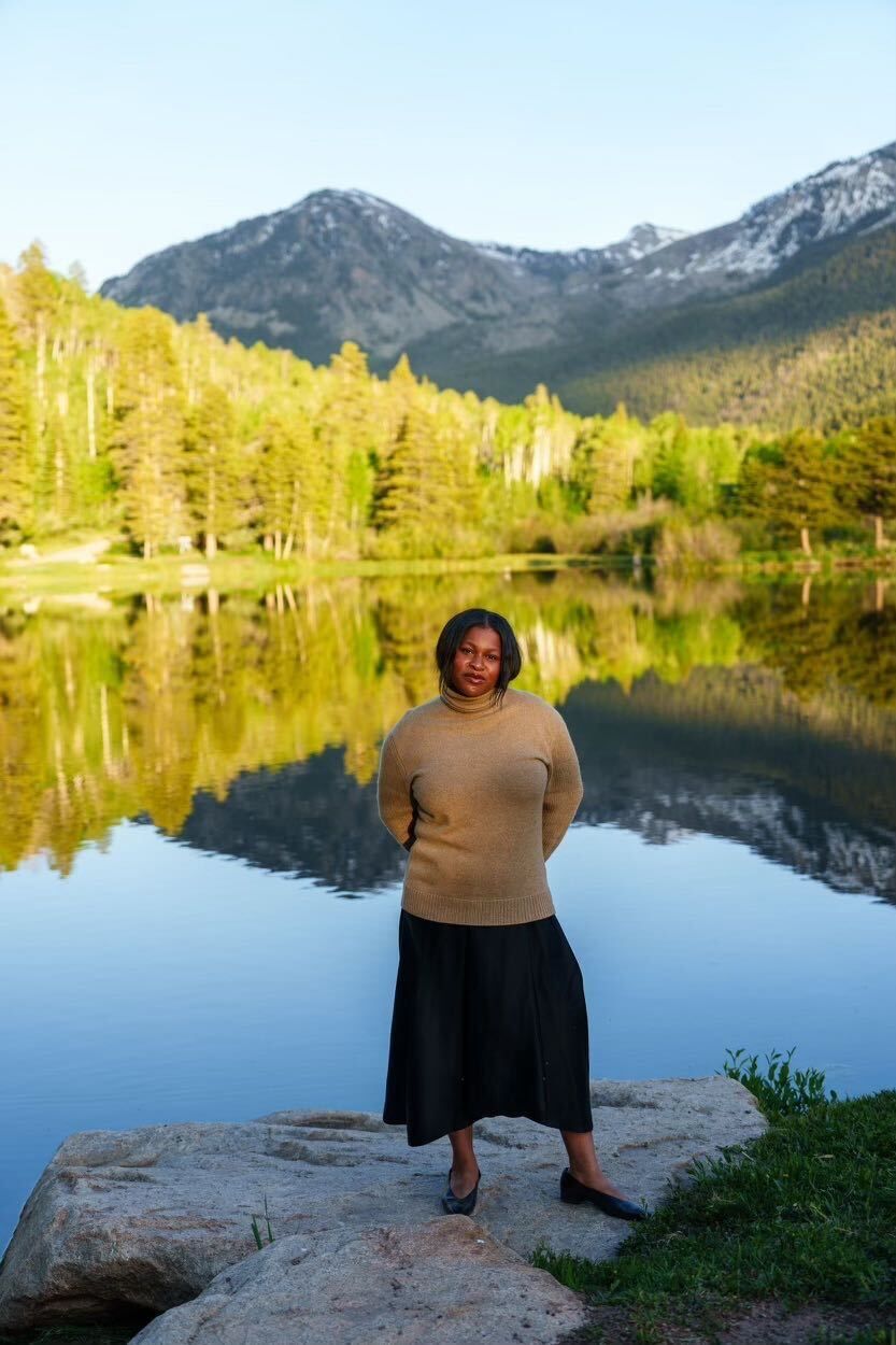 a woman standing on a rock by a lake with trees and mountains in the background