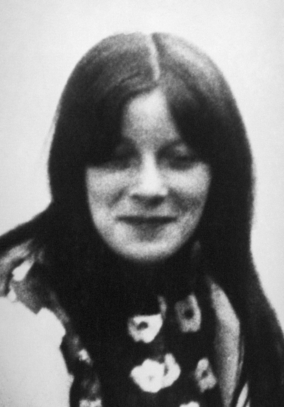 a young woman smiles at the camera with closed eyes, she wears a patterned sleeveless shirt