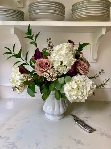 flowers arranged in a white vase on a marble surface infront of a white wall