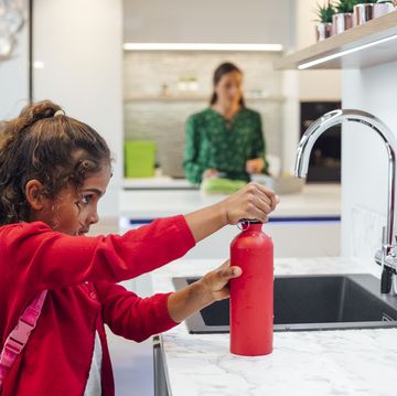 a girl holding a red water bottle next to a sink