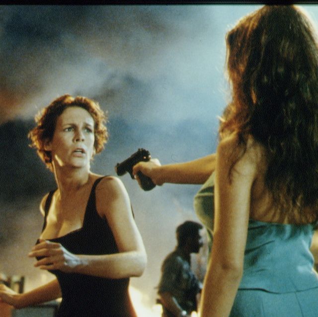 a publicity photo from the movie true lies, featuring jamie lee curtis reacting with concern as a woman points a gun at her