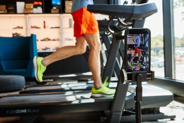 a person running on a treadmill with a phone on a tripod filming