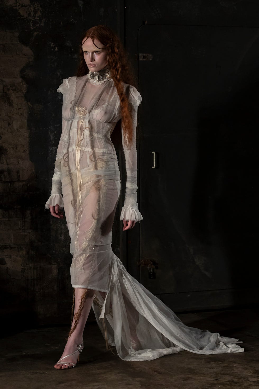 Fashion model wearing a sheer white dress with intricate detailing and a long train in an industrial setting