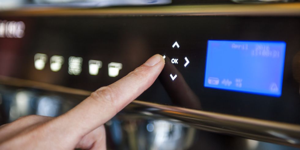 finger pushing digital button on coffee machine