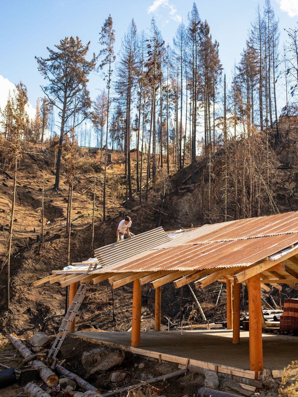 In Lago Puelo Argentini brengt een bouwvakker plaatmateriaal aan op het dak van een huis dat wordt hersteld Het huis staat op een voormalige dennenplantage die tijdens de bosbrand van 9 maart 2021 tot de grond toe afbrandde