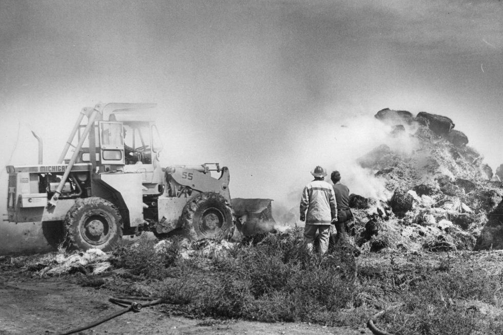 firefighters battle a blaze in a haystack with a tractor to the left